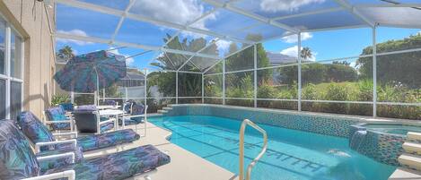 A covered outdoor swimming pool with lounge chairs and an umbrella.