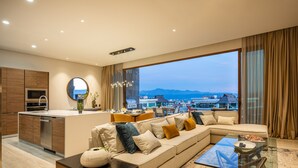 Una sala de estar moderna con un ventanal grande, un sofá, una mesa de centro de vidrio y una zona de cocina.