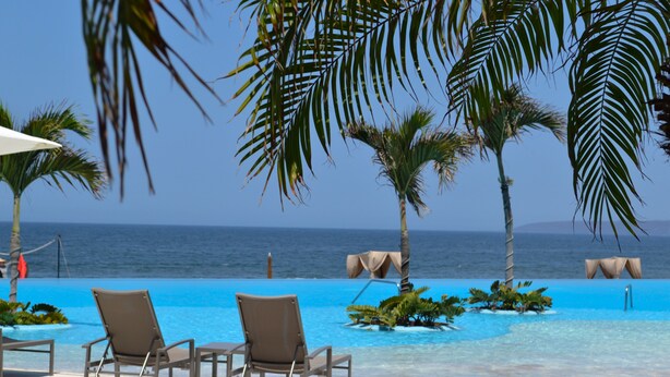Zona de piscina con sillones de descanso y vista al océano.