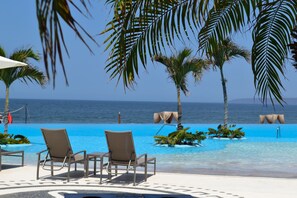 Zona de piscina con sillones de descanso y vista al océano.