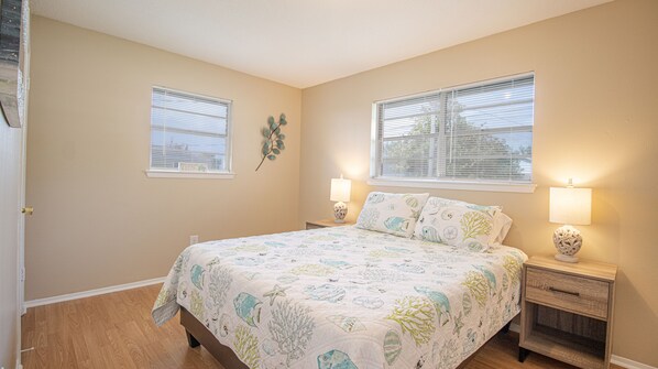 A bedroom with a bed, two bedside tables, two lamps, and two windows with blinds.