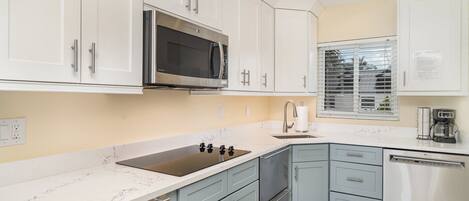A modern kitchen with white cabinets, a stainless steel microwave, a sink, and a dishwasher.