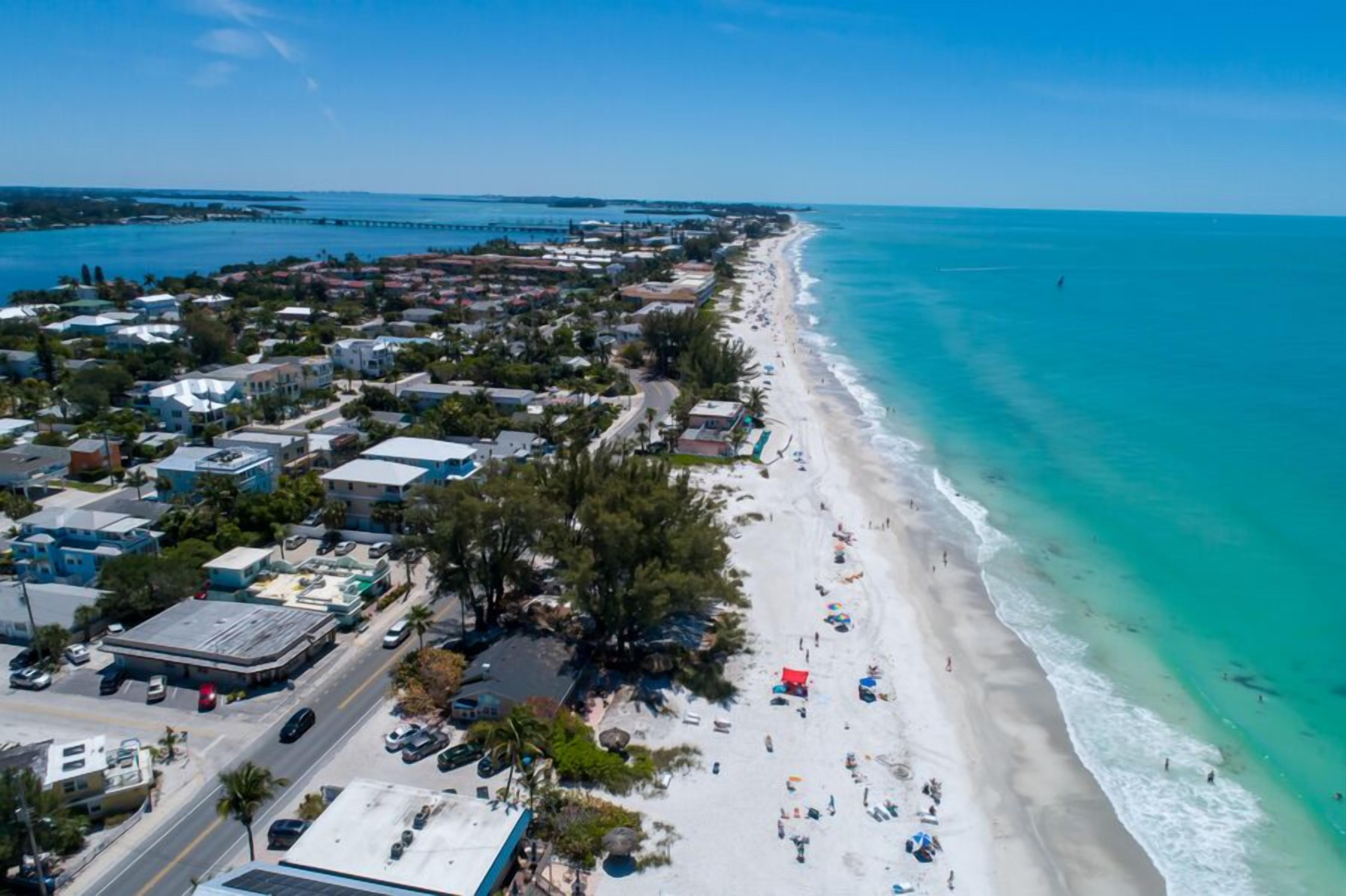 A coastal town with a long beach, clear blue waters, and a mix of residential and commercial buildings along the shore.