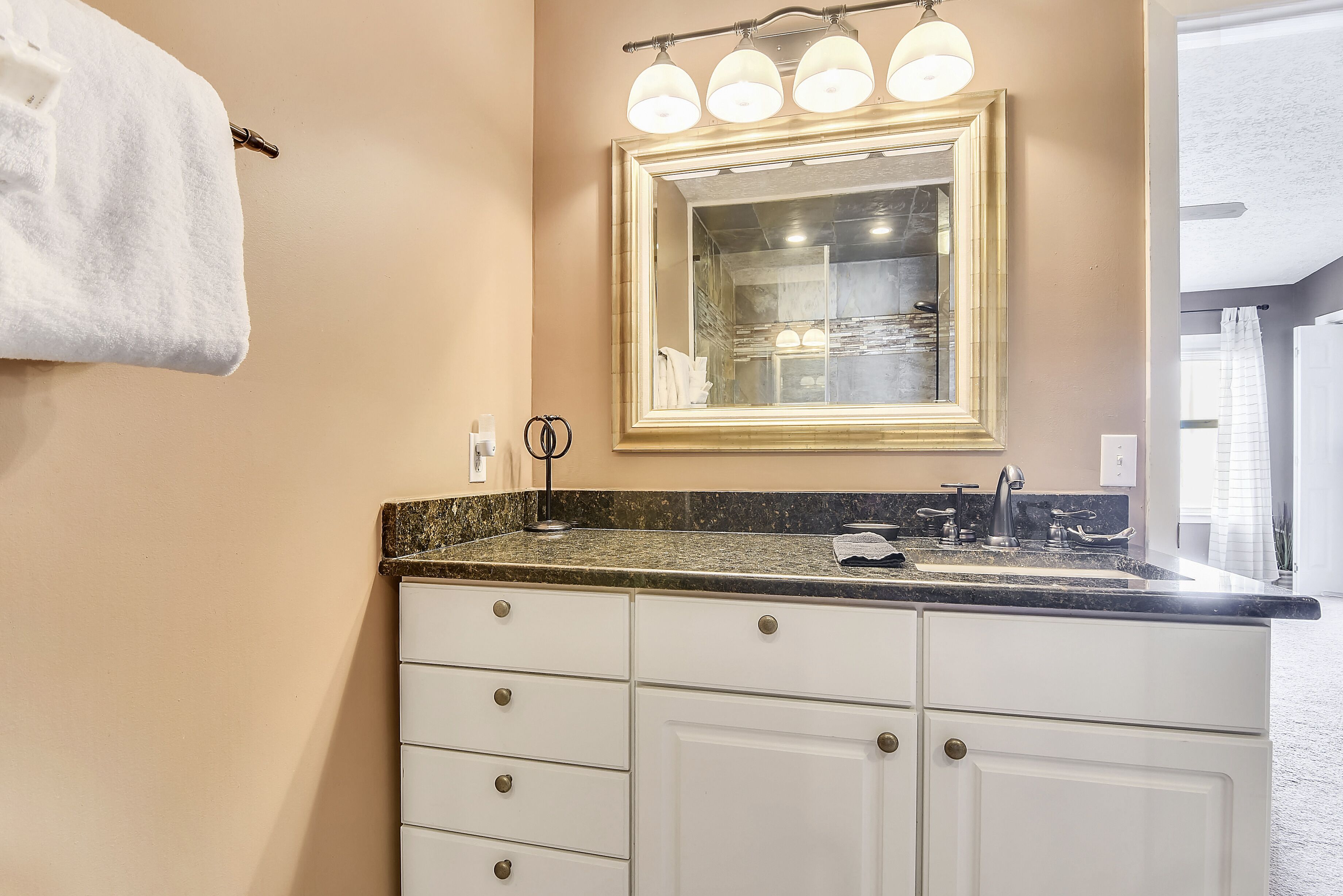 A bathroom with a sink, mirror, and white cabinets.