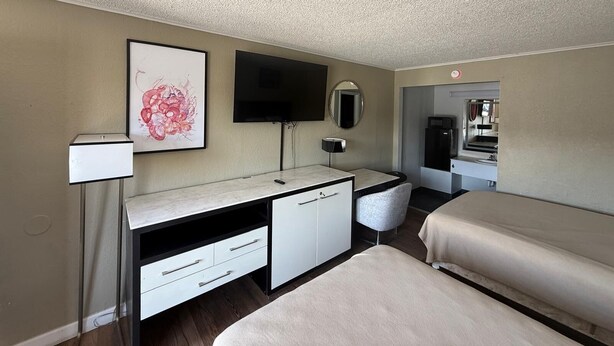 A hotel room with a bed, a desk with a chair, a flat-screen TV, a mirror, and a framed artwork on the wall. - I-26 Inn (Johnson City)