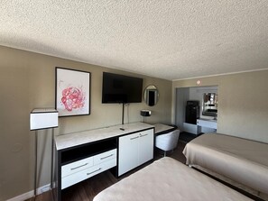 Une chambre d’hôtel comprenant un lit, un bureau avec une chaise, un téléviseur à écran plat, un miroir et une œuvre d’art encadrée accrochée au mur.