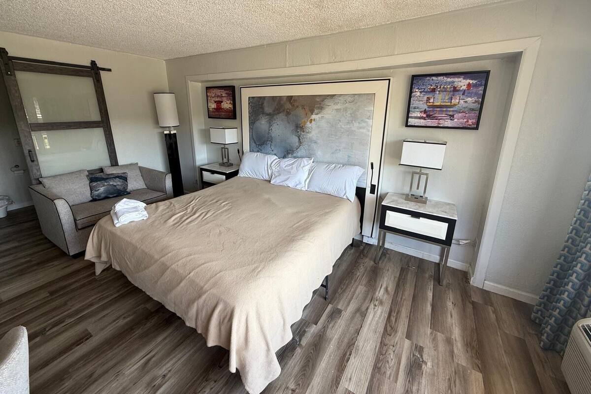A hotel room with a large bed, a sofa, two nightstands, and a mirror.