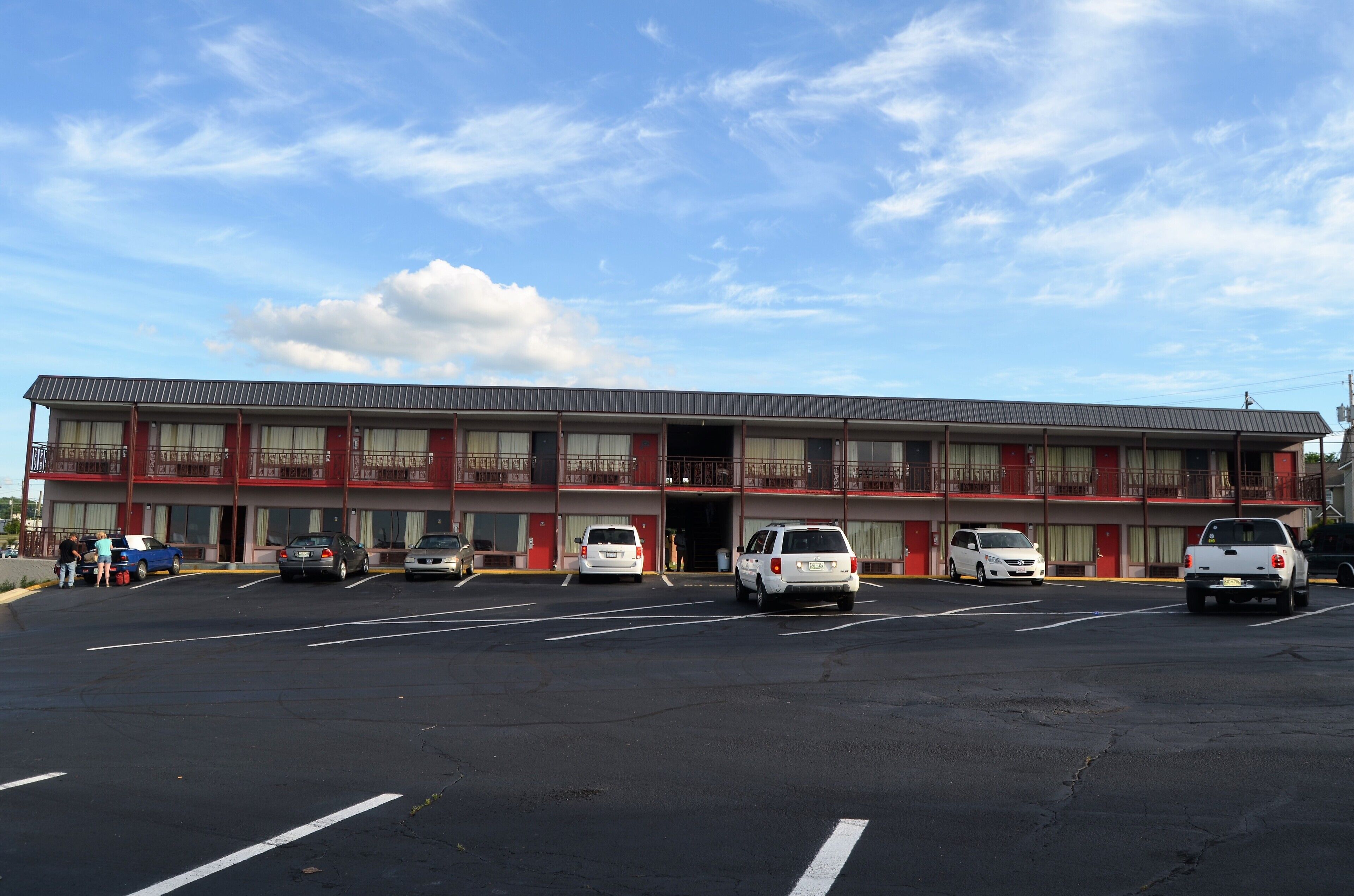 Un motel con fachada roja, varios balcones y un estacionamiento con varios coches.