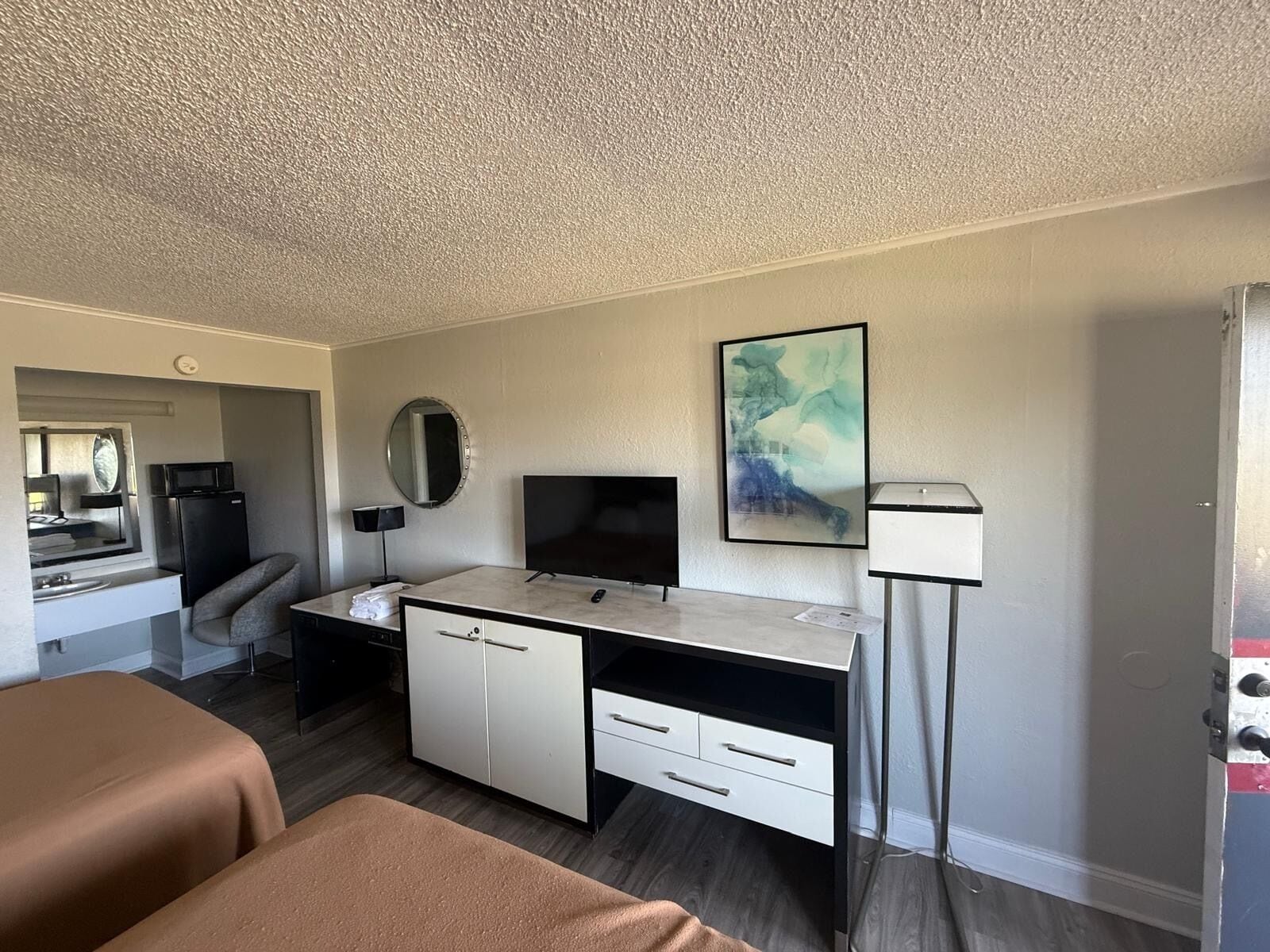 A modern hotel room with a desk, a flat-screen TV, a large abstract painting, a bedside lamp, and a bed.