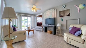 A spacious living room with a sofa, a glass coffee table, a TV, and a ceiling fan. - Seas The Day in Cudjoe Key (Cudjoe Key)