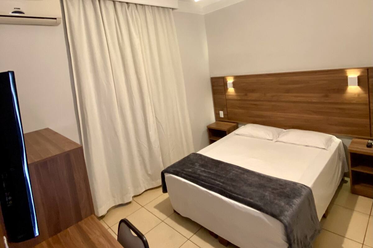 Ett hotellrum med en säng, ett skrivbord, en stol, en takfläkt och en TV.