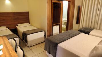 Habitación de hotel con tres camas individuales, cabecera de madera, una mesita y televisor montado en la pared.