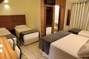 Habitación de hotel con tres camas individuales, cabecera de madera, una mesita y televisor montado en la pared.