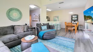 A living room with a gray sofa, a coffee table, and a blue rug. There is a dining area with a wooden table and chairs.