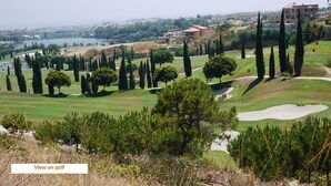 A golf course with sand bunkers, a pond, and a view of a city in the distance.
