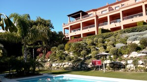 A hotel with a swimming pool, surrounded by lush greenery and a rocky hillside.