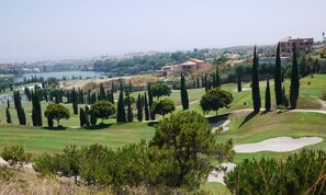 Un campo de golf con bunkers de arena, un estanque y una vista de una ciudad al fondo.