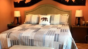 Ein Schlafzimmer mit einem großen Bett, zwei Nachttischen mit Lampen, einer Bank und einer Wand mit Bär-Motiv.