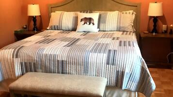 Une chambre avec un grand lit, deux tables de chevet avec des lampes, un banc et un mur décoré avec un motif d’ours.