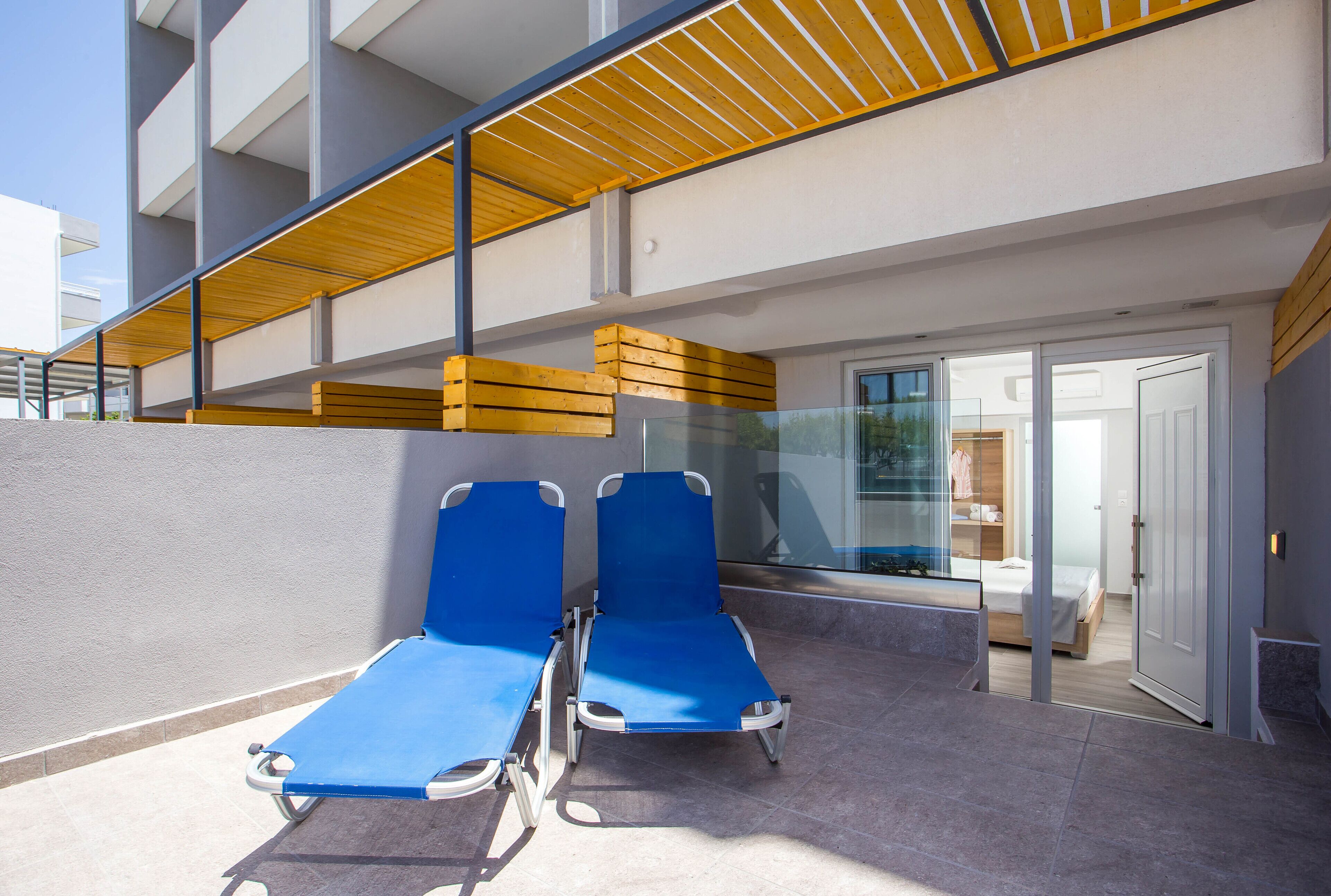 A balcony with two blue lounge chairs, a wooden ceiling, and a glass door leading to a bedroom.