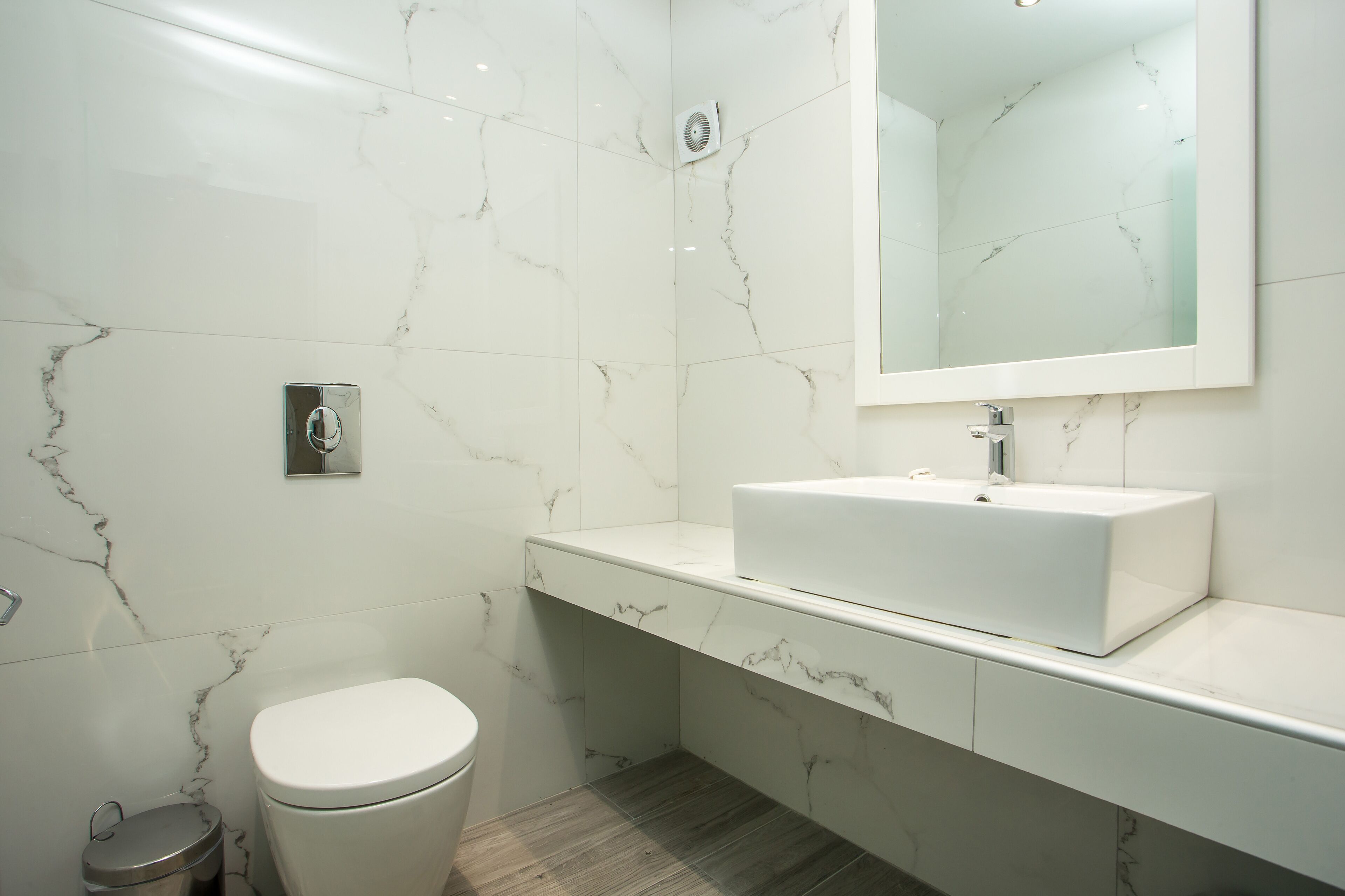 A modern bathroom with a white marble wall, a white sink, and a toilet.