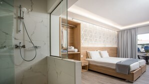 Une chambre d’hôtel moderne dotée d’une douche, d’une tête de lit en bois, d’un lit avec une couverture grise et d’une grande fenêtre avec des rideaux.