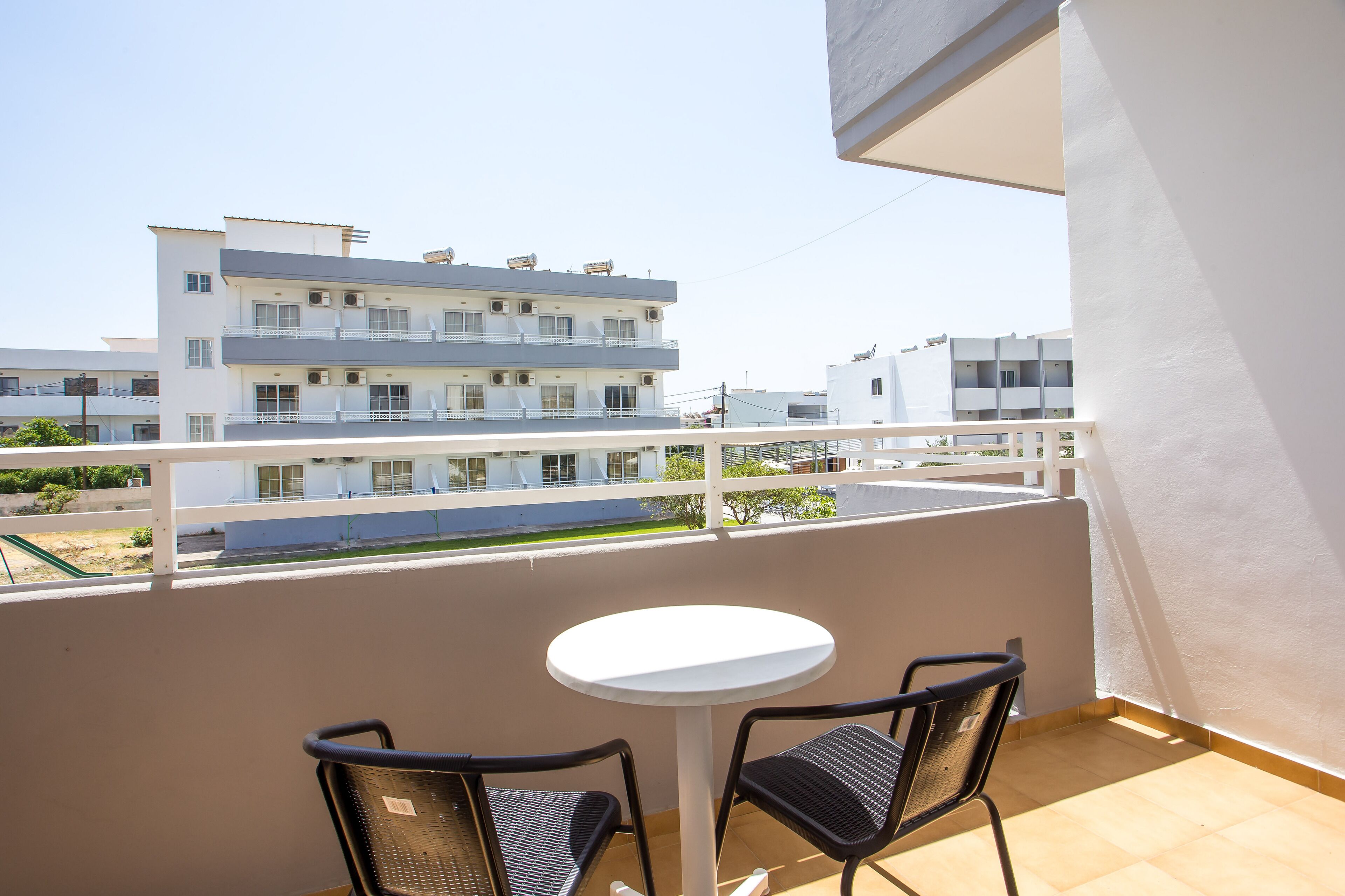 A balcony with a white table and two chairs, overlooking a residential area with multi-story buildings.