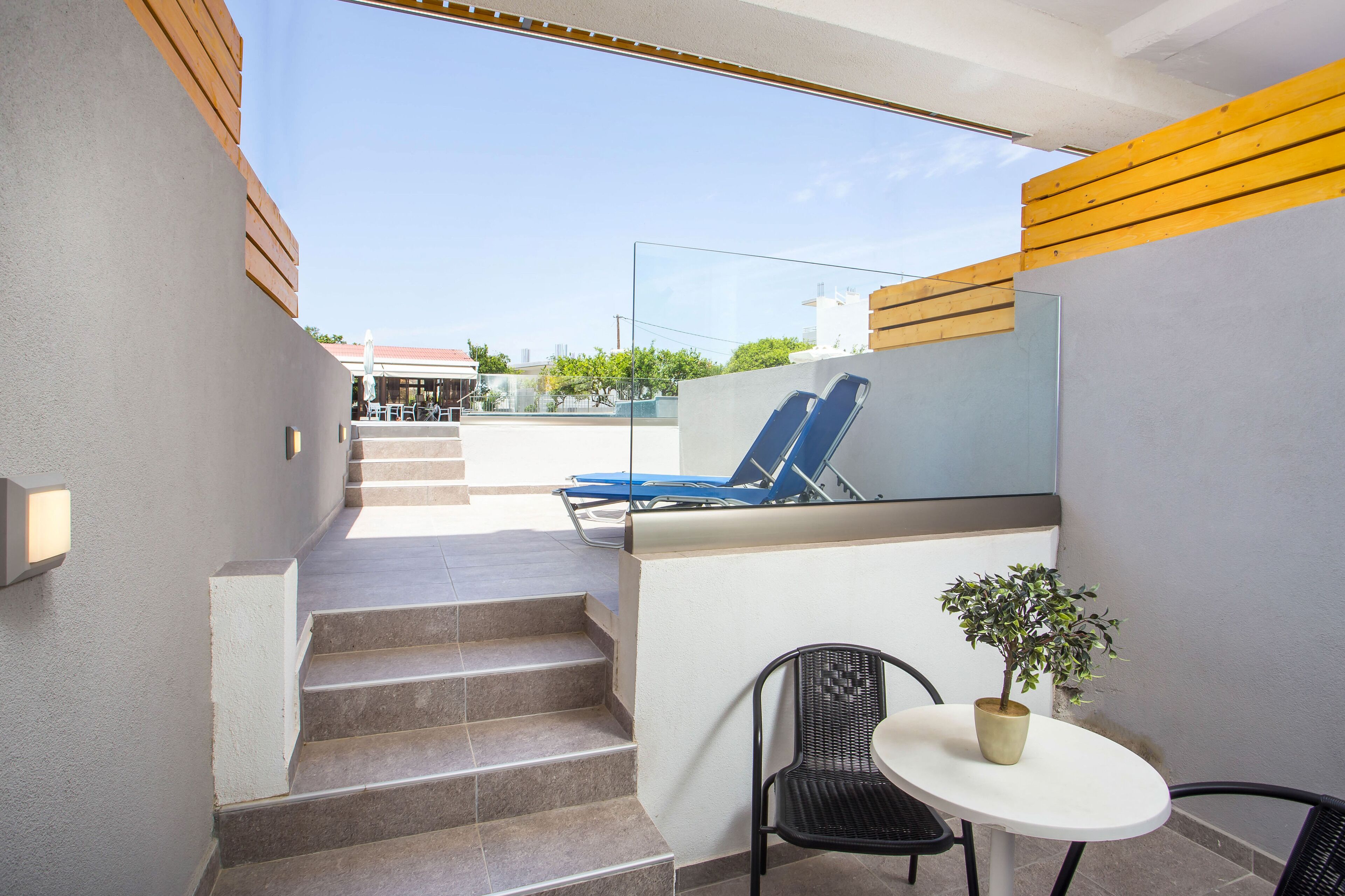 A modern outdoor area with a staircase leading to a balcony, a seating area with a table and chairs, and a potted plant.