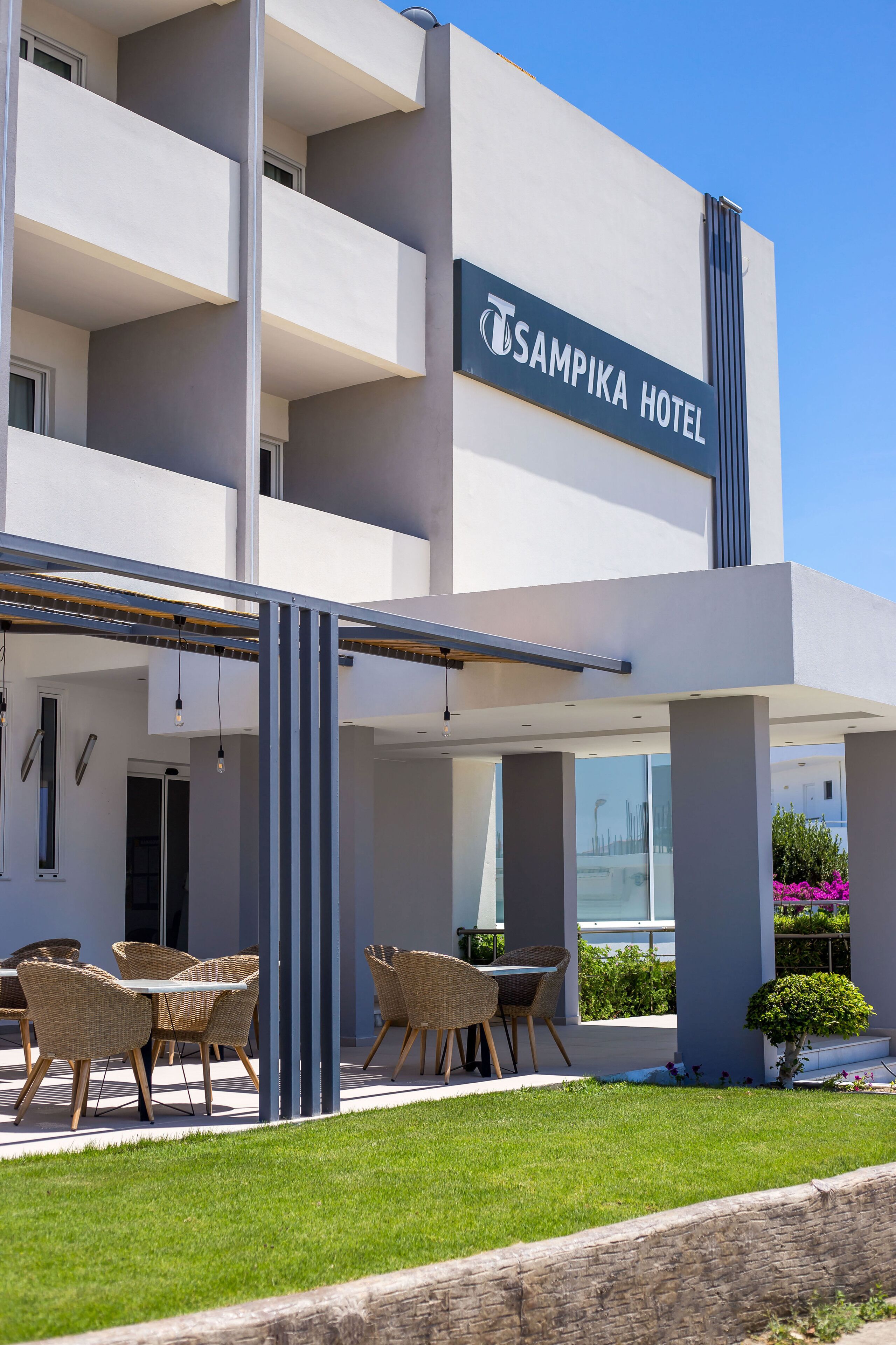 A modern hotel with a sign reading 'SAMPIKA HOTEL' and outdoor seating area with wicker furniture.