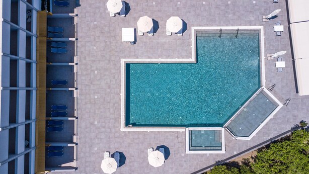 Vue aérienne d’un espace piscine sur le toit, avec une piscine rectangulaire, des chaises longues et des parasols.