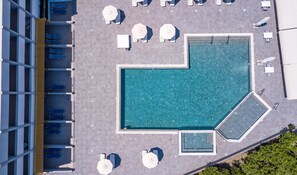 Vue aérienne d’un espace piscine sur un toit, avec plusieurs chaises longues et parasols.