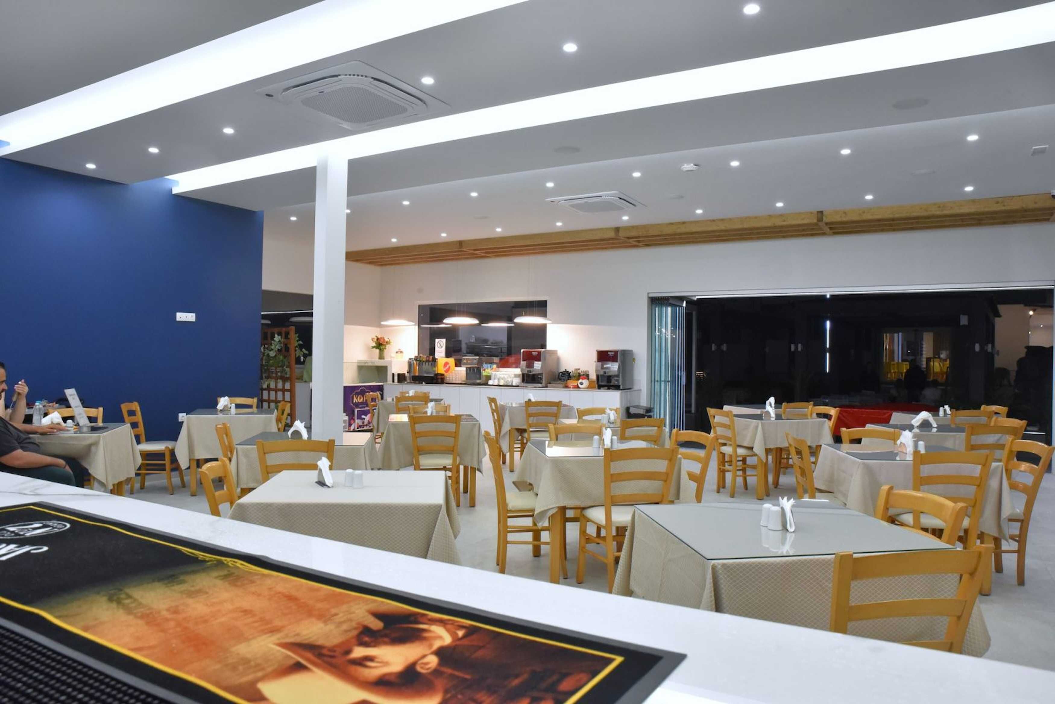 A restaurant with multiple tables and chairs, a counter with a menu, and a kitchen area in the background.