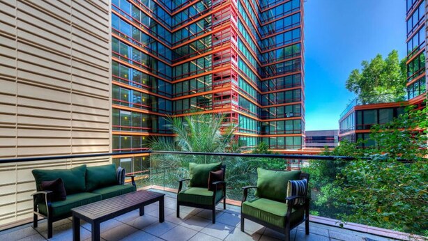 A modern outdoor seating area with a sofa and chairs, a wooden table, and a view of tall buildings with red accents. - Condo magnifico in the heart of the Biltmore (Phoenix)