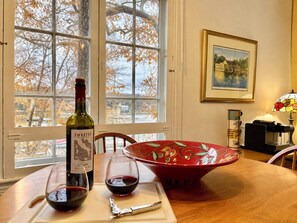 Une table à manger avec une bouteille de vin, des verres et un bol rouge orné d’un motif de feuilles.