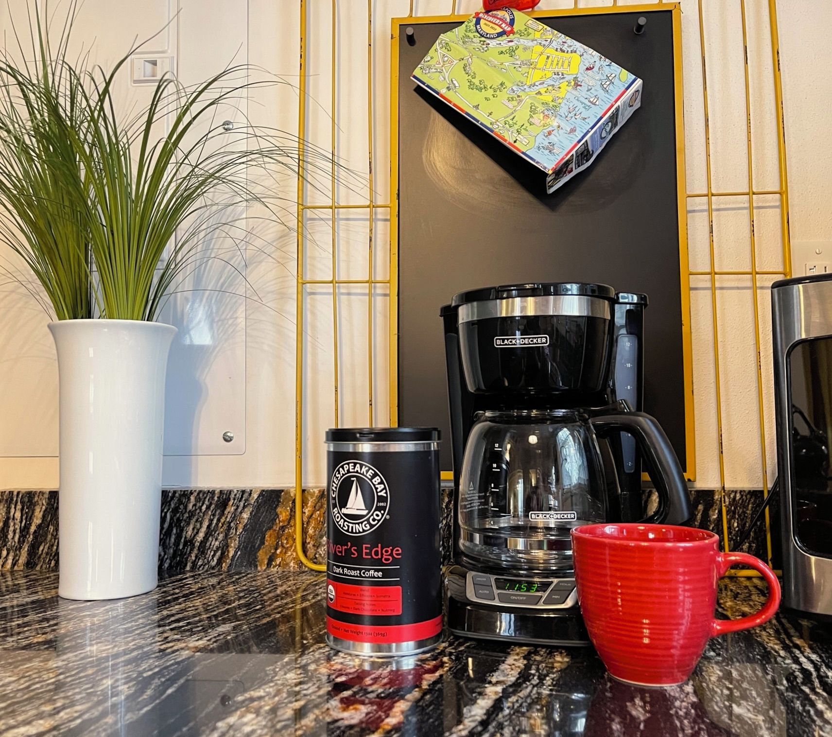 A kitchen counter with a coffee maker, a can of coffee, a red mug, and a potted plant.