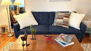 A living room with a blue sofa, two lamps, a framed picture, and a coffee table with decorative items.