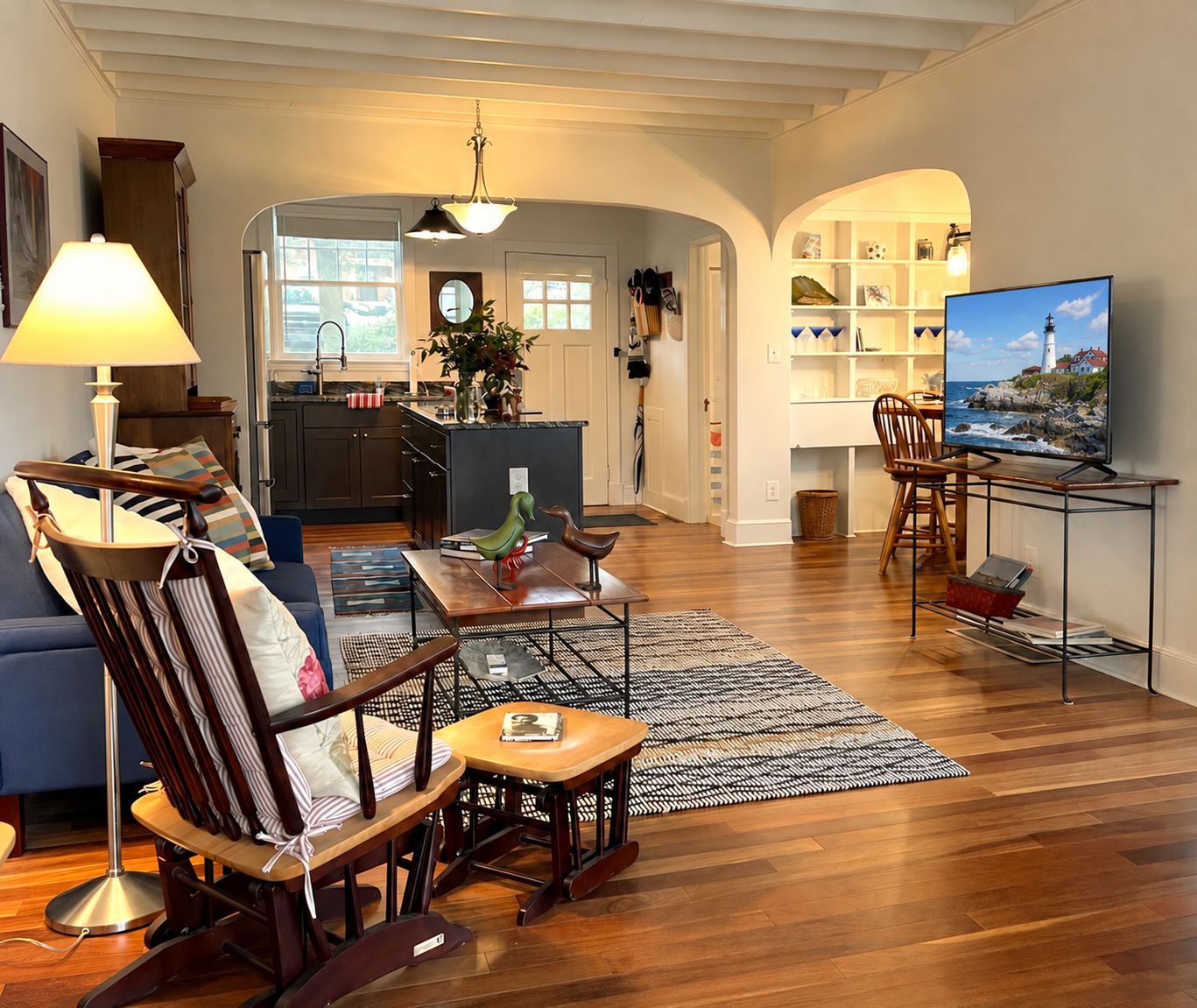 A living room with a TV, a dining area, and a kitchen in the background.