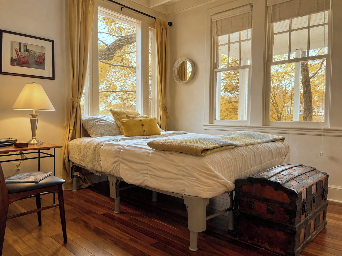 Une chambre à coucher avec un lit, une table de chevet avec une lampe, une chaise et une malle.
