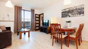 Un salon moderne avec une table à manger en bois, des chaises, un canapé, un téléviseur et un tableau représentant un paysage urbain accroché au mur.