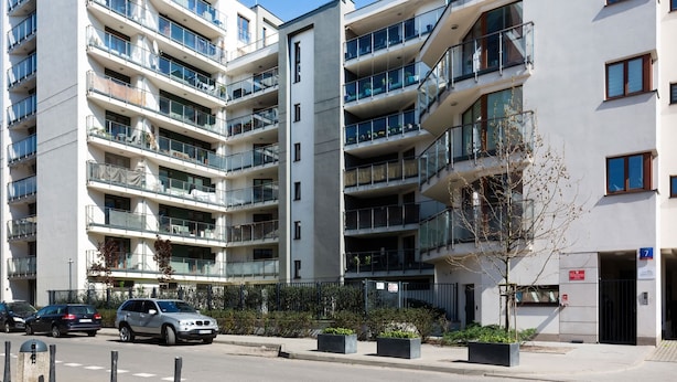Un immeuble résidentiel moderne à plusieurs étages, doté de balcons, d’une entrée sécurisée et surplombant un ciel dégagé.