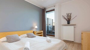 Un lit bien fait, avec une serviette pliée, une lampe de chevet et une vue sur un balcon à travers une porte vitrée.
