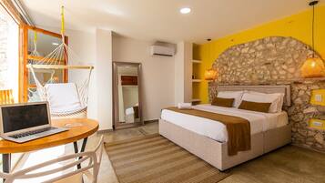 A bedroom with a bed, a desk with a laptop, a hammock, and a stone wall.