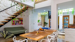 A spacious living area with a wooden dining table, white chairs, a green sofa, and a staircase with plants. - Fun House, Pool & Rooftop, Best Location Getsemani (Cartagena)