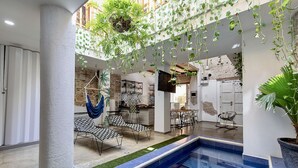 An indoor pool area with hanging plants, a hammock, and a dining area with chairs and tables. - Fun House, Pool & Rooftop, Best Location Getsemani (Cartagena)