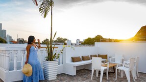 A rooftop terrace with a white outdoor seating area, a potted plant, and a city skyline in the background. - Fun House, Pool & Rooftop, Best Location Getsemani (Cartagena)
