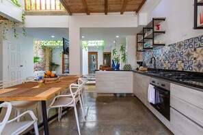 Une cuisine moderne avec un coin repas, comprenant une table en bois, des chaises blanches et un îlot de cuisine doté d’un évier et d’une cuisinière.