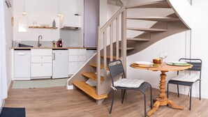 A modern kitchen with white cabinets, a built-in oven, and a wooden staircase leading to a dining area with a round wooden table and two chairs.