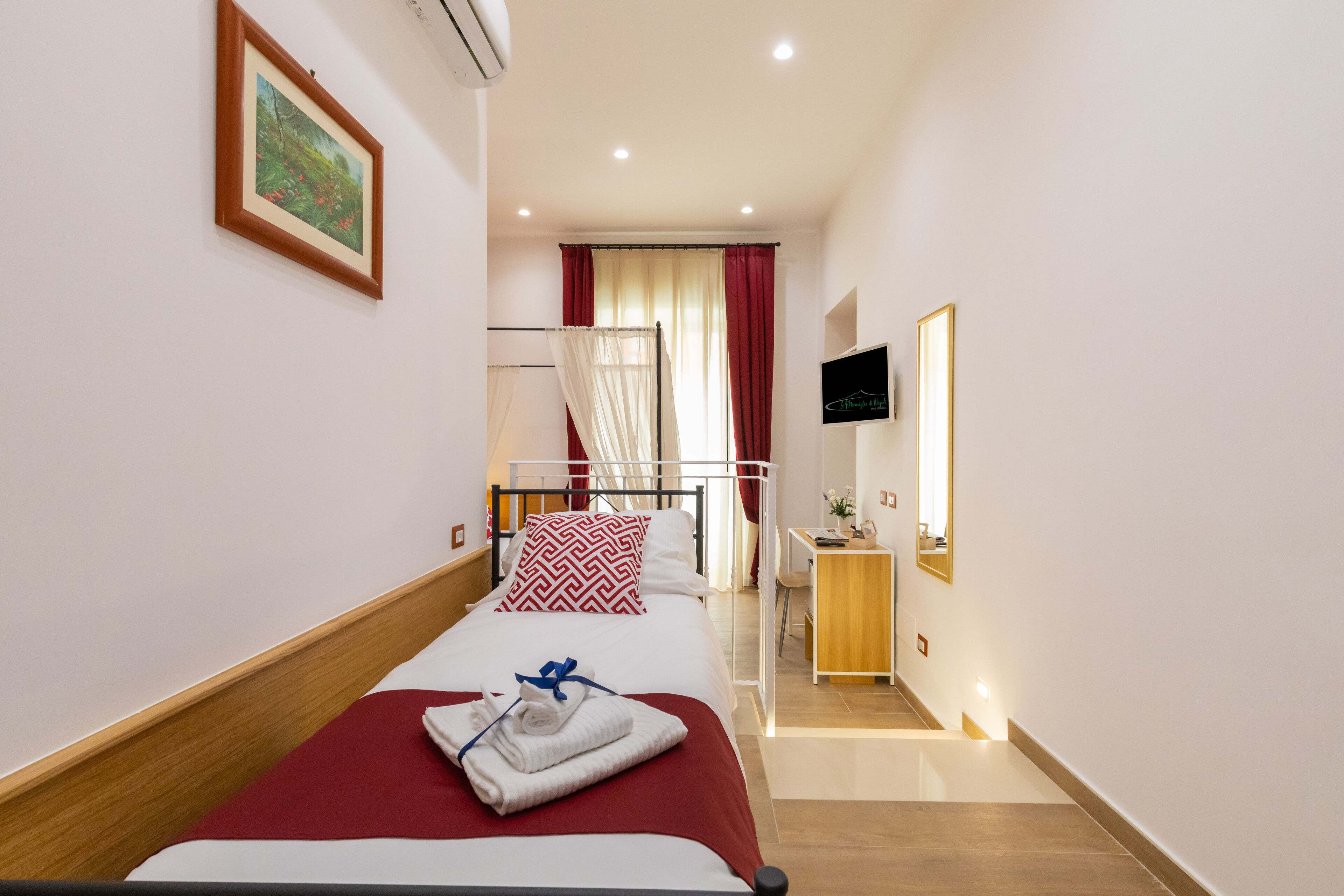 A hotel room with a bed, a desk, a TV, and a window with curtains.