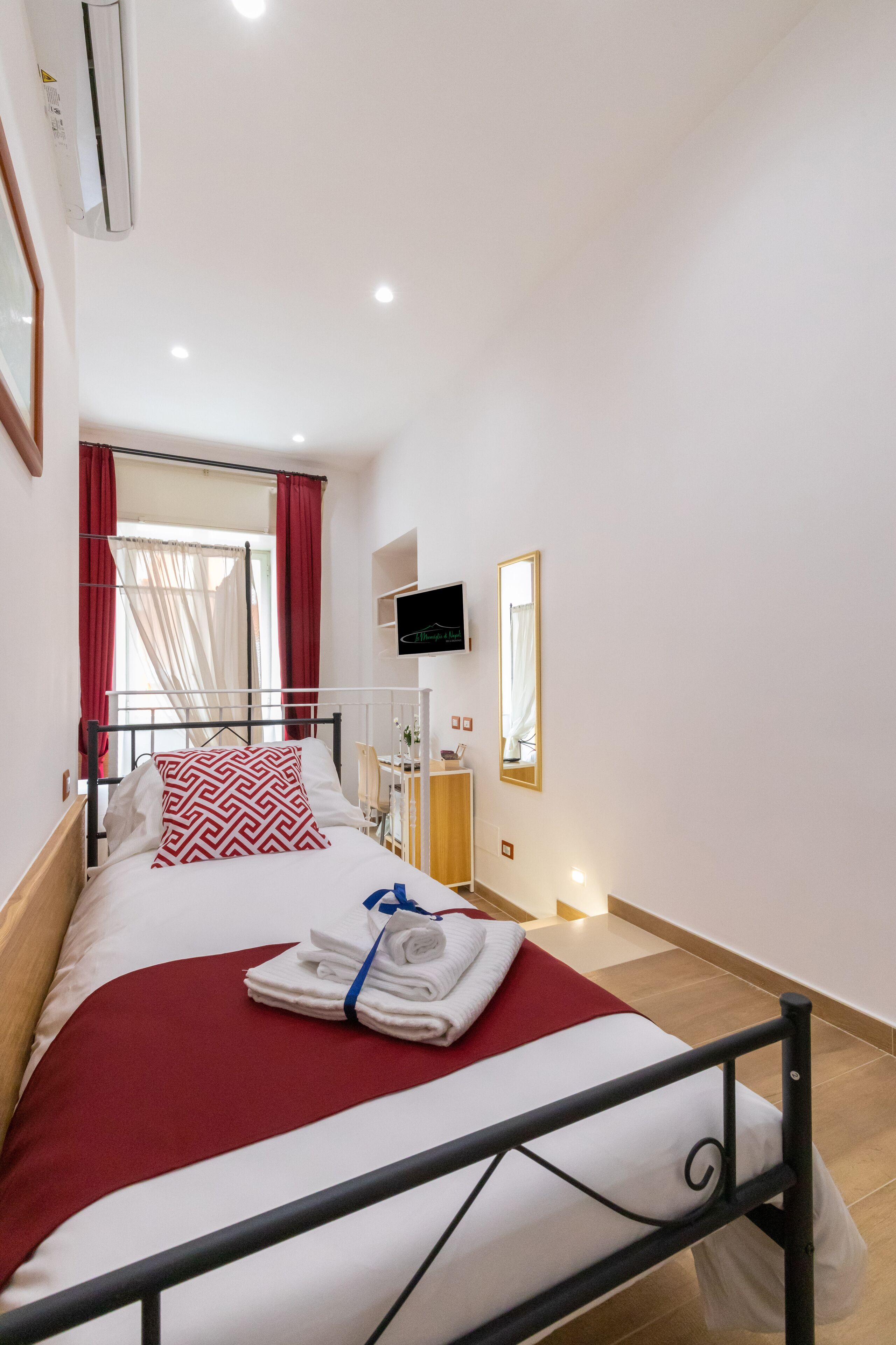 A hotel room with a bed, a TV, a mirror, and a window with curtains.