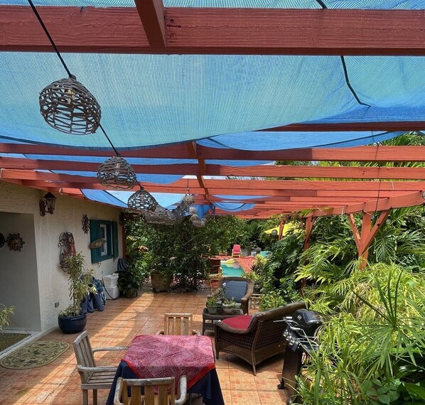 Un patio cubierto con mobiliario exterior, una parrilla y plantas en macetas.